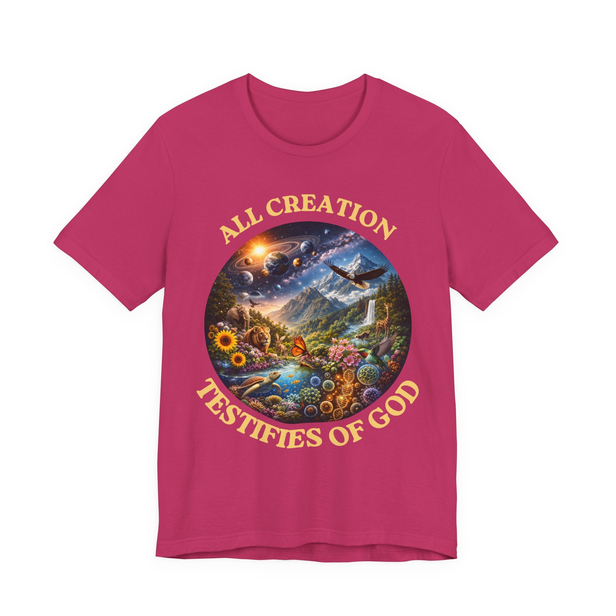 A bright pink short-sleeve t-shirt with a circular multicolor graphic on the chest. The graphic features a scenic landscape with a waterfall, mountains, and a bird, surrounded by the text 'ALL CREATION TESTIFIES OF GOD' in a gold/yellow font.